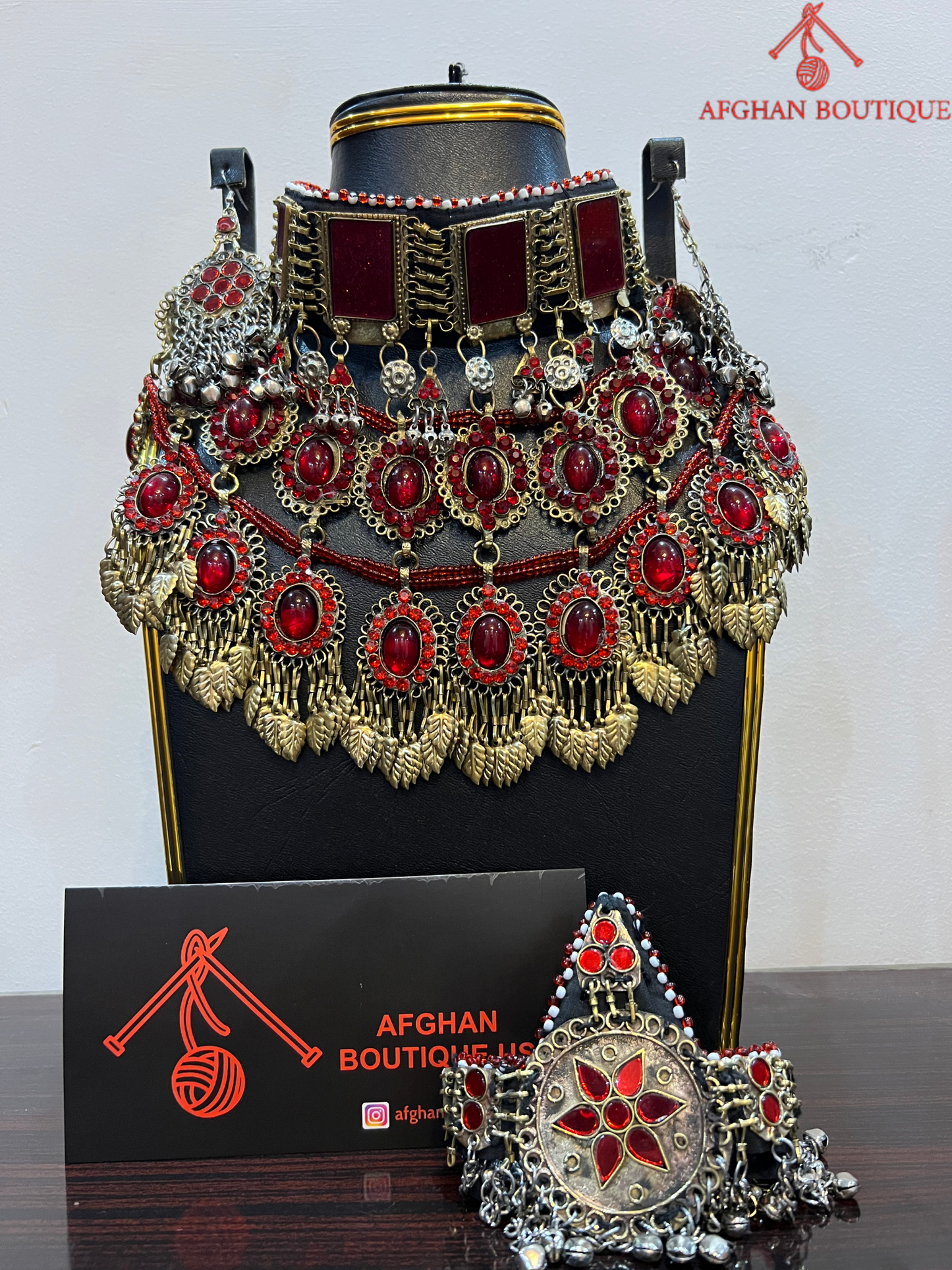 Decorative headpiece with red and gold details on a black stand, branded 'Afghan Boutique'.