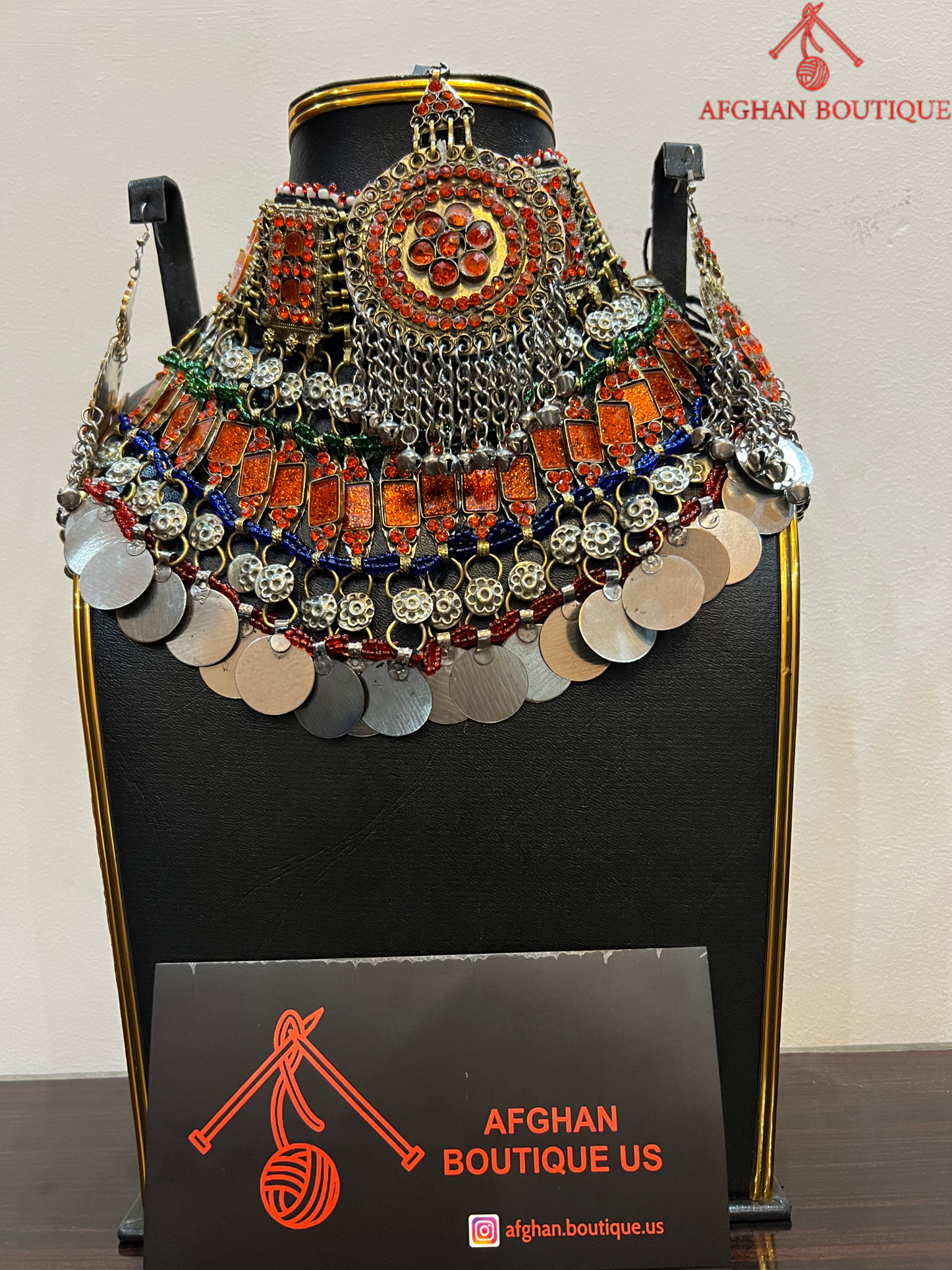 Decorative headpiece with coins and beads on a stand with 'Afghan Boutique US' branding.