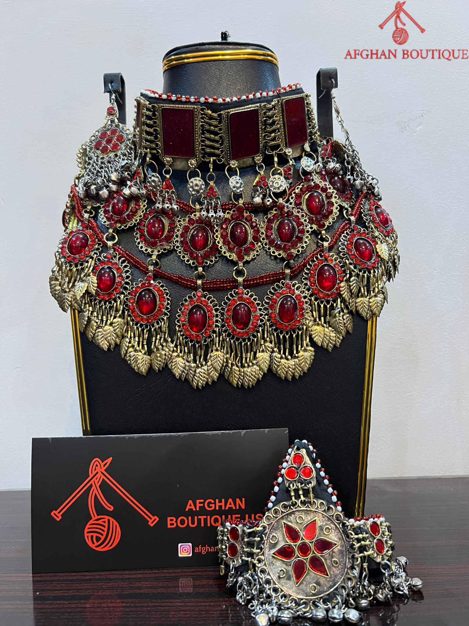 Decorative headpiece with red and gold details on a black stand, branded 'Afghan Boutique'.